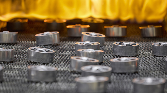 Round powder metal parts entering a sintering oven.