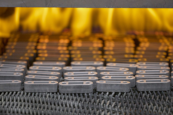 Small iron parts entering a sintering oven.