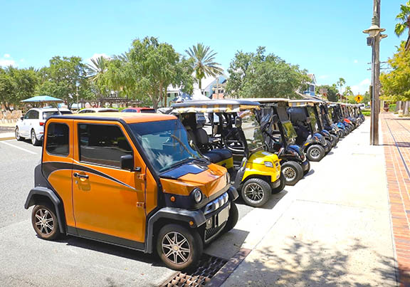 Multiple golf carts parked along the curb in a city's downtown.