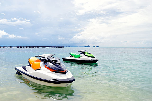 Two jet skis, or personal watercraft, sit unmanned in the shallows on a sunny day.