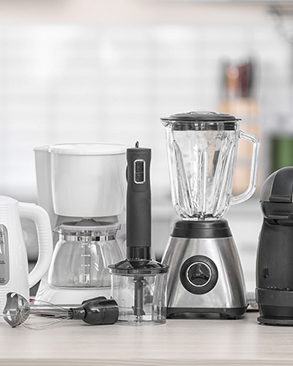 Common household kitchen appliances are lined up on a countertop.