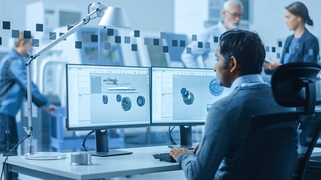 An engineer sits at his desk looking at part blueprints and designs on this 2 computer monitors.