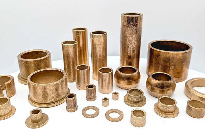 Assorted bronze bearings, sleeve bushings and thrust washers lined up against a white background.
